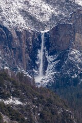 Bridalveil Fall cascades down granite cliffs in Yosemite National Park, USA. Snow dusts the...