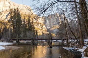 Hikers cross a bridge over the Merced River in Yosemite National Park, USA. The granite cliffs and...