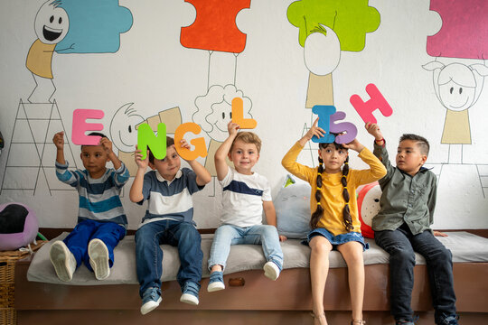 Diverse group of preschool children holding large colorful letters spelling “English” in a bright classroom. Early language learning, playful literacy, preschool and kindergarten education