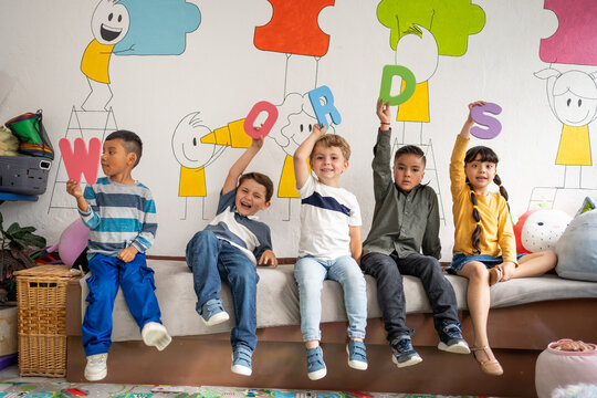 Diverse group of preschool children holding large colorful letters spelling “Words” in a bright classroom. Early language learning, playful literacy, preschool and kindergarten education