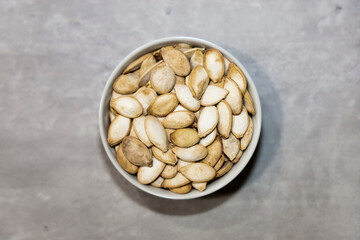 Top view of unhulled roasted and salted pumpkin seeds in a small white bowl for snacking.