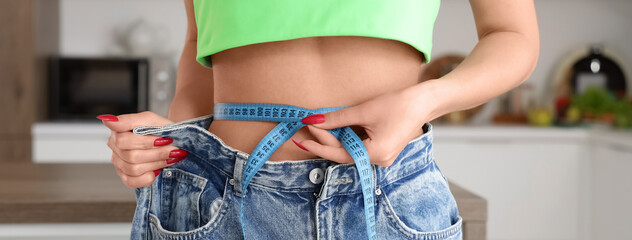 Young woman in loose jeans measuring waist at home, closeup. Diet concept