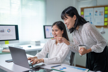 Two women are working on a laptop together, one pointing at a screen