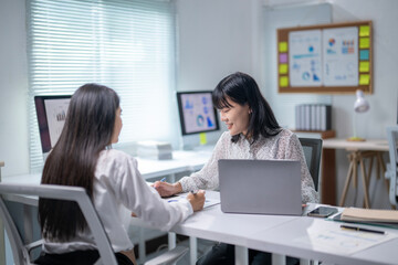 Two women are sitting at a desk, talking to each other