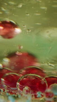 Vertical video. Defocused diffusion oil. Drops gel. Sedimentation red bubbles bottom. Mixing air liquid different density. Sink droplet. Chemical process closeup.