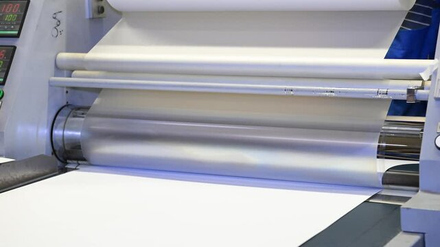 An industrial laminator works by laminating, applying a transparent film to paper in the production room of a printing house