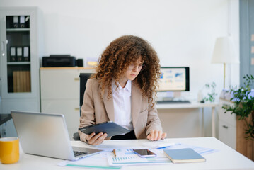 Obraz premium businesswoman reviewing analytics on tablet at bright office desk with charts, laptop, and documents. Concept of data planning