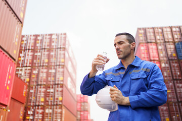 Container yard worker is taking a break and drinking water during a very hot day.