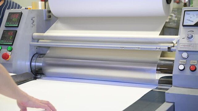 An industrial laminator works by laminating, applying a transparent film to paper in the production room of a printing house