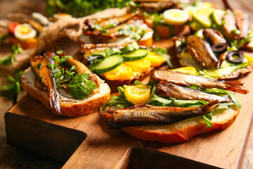 Wooden board of tasty sandwiches with canned smoked sprats on table