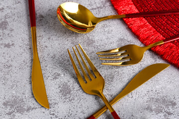 Golden set of cutlery with red handles on grey background