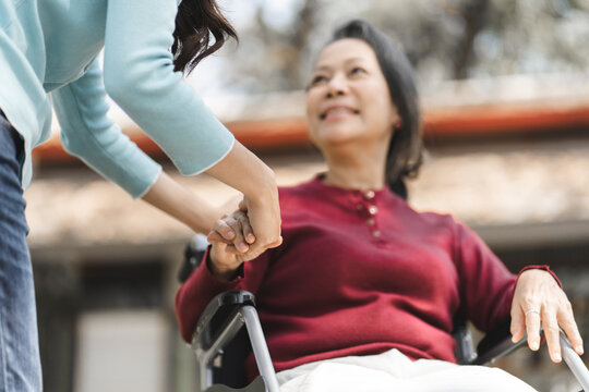 Family relationship Asian senior woman in wheelchair with happy daughter holding caregiver for a hand while spending time together