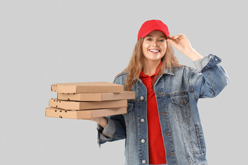 Female courier holding many pizza boxes on grey background