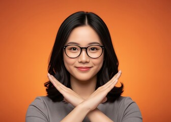 Young Asian Woman Wearing Glasses Makes X Sign with Arms Standing Against Orange Background