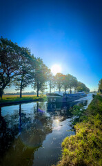 A beautiful picturesque scene of a charming canal adorned with lush trees, reflective waters, and a...