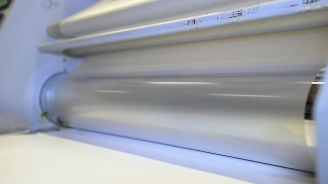 An industrial laminator works by laminating, applying a transparent film to paper in the production room of a printing house