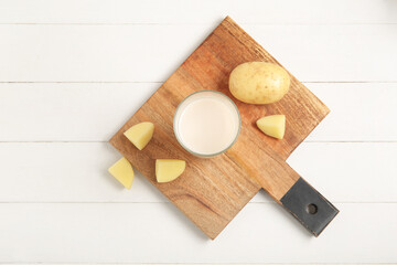 Glass of tasty potato milk on white wooden background