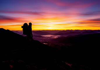 Silhouetted hiker admires vibrant sunrise over a vast mountain valley.