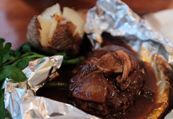 Osaka, March 24, 2024 – Hamburger steak with brown onion sauce served on foil with baked potato and green vegetables on the side.