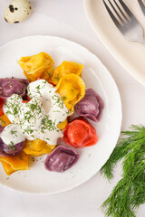 Plate of boiled colorful dumplings with sour cream and dill on white background