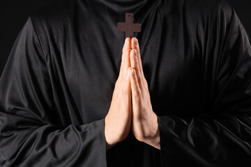 Young priest with cross praying on black background, closeup