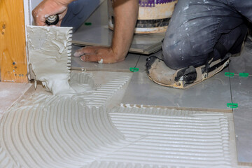 Worker is spreading tile adhesive on floor in home renovation project, preparing for tile installation.