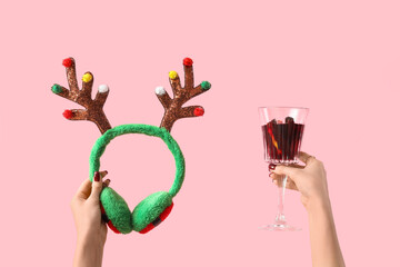 Female hands with glass of warm mulled wine and Christmas reindeer horns on pink background