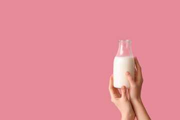 Hands holding bottle of milk on pink background