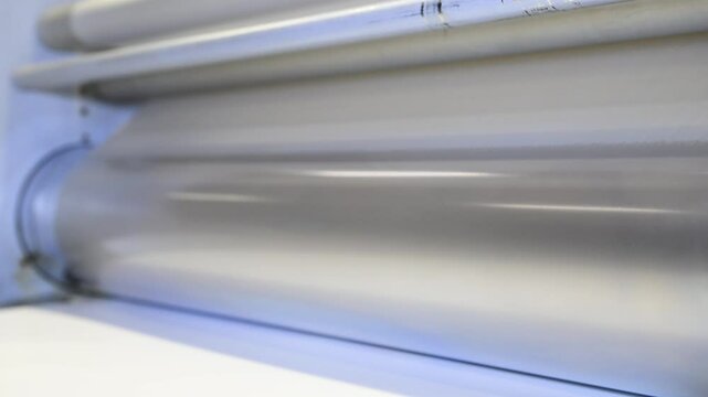 An industrial laminator works by laminating, applying a transparent film to paper in the production room of a printing house