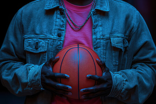 A person in a denim jacket grips a red-black basketball under intense blue light, A powerful portrait of a player cradling a basketball, emanating strength and dedication.