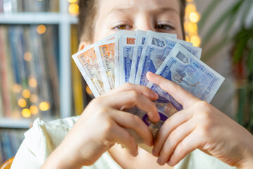 child 10 years old, primary school student presenting British GBP banknotes currency in hand,...