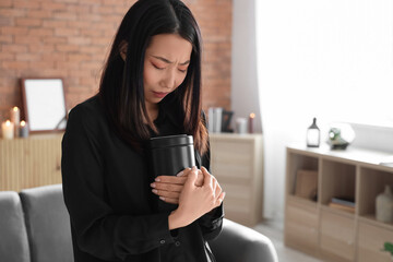 Grieving young Asian woman with mortuary urn at funeral