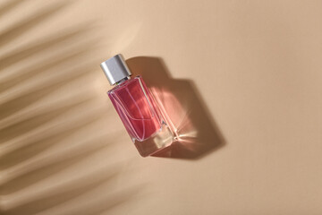 Pink bottle of perfume with shade of palm branch on beige background. Top view