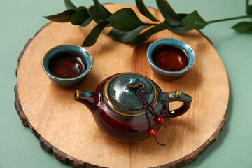 Wooden stand with teapot, cups of tasty tea and leaves on olive background
