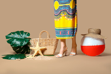Young woman with wicker bag, palm leaves and beach ball on beige background. Summer vacation concept