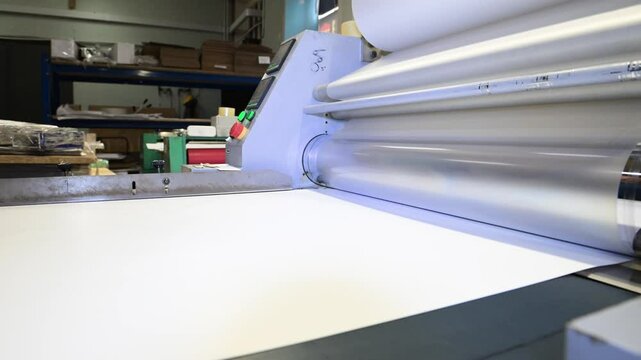 An industrial laminator works by laminating, applying a transparent film to paper in the production room of a printing house