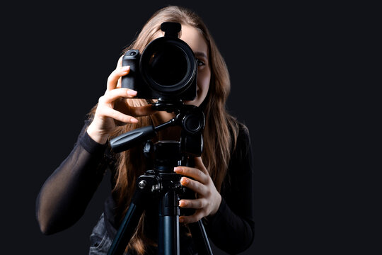 Female photographer with modern camera on tripod taking picture of viewer against black background