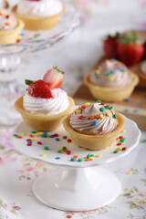 Delicious mini tarts with creamy toppings and colorful sprinkles, one is topped with fresh strawberries