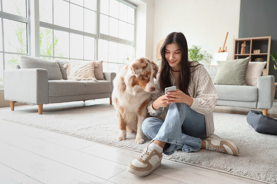 Young woman with Australian Shepherd dog using mobile phone at home