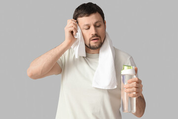 Sporty young man with bottle of water wiping sweat on light background