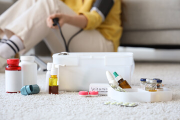 First aid kit with medications of woman measuring blood pressure at home, closeup