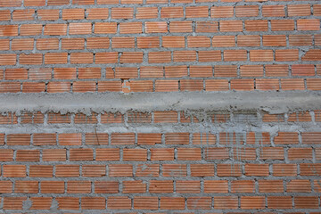 A partially constructed red brick wall with visible grey mortar and steel reinforcing bars (rebar), indicating