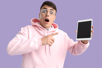 Shocked young man pointing at blank tablet computer on lilac background