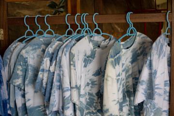 close-up shot of tie-dye t-shirts hanging on light blue plastic hangers. The shirts feature a soft, pastel tie-dye pattern.