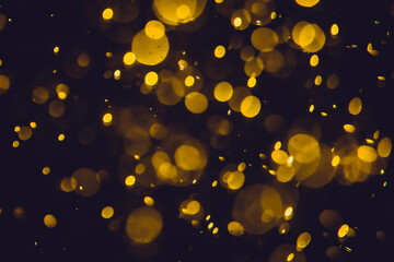 Defocused  golden bokeh lights in various sizes and colors on a dark background creating a dreamy and abstract visual effect