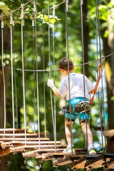 Child with harness crossing a rope bridge in a fun adventure park for kids. Outdoor forest activity focused on balance, courage, and safety. Adventure park with kids sport activities.