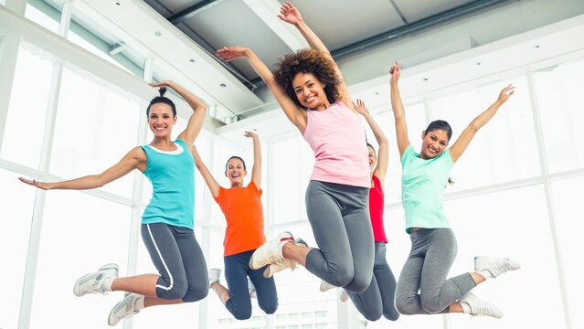 Five women are jumping inside flat design fitness studio with glass windows and vibrant activewear