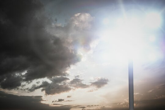 Fototapeta Metal lamp post with glowing fixture is radiating lens flares in flat design under dramatic clouds