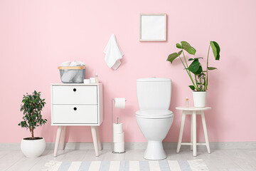 Toilet bowl, bedside table and plants near pink wall in restroom