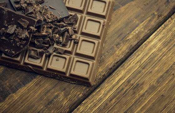 Naklejki Flat vector milk chocolate bar is resting on weathered plank, revealing dark shards and shavings